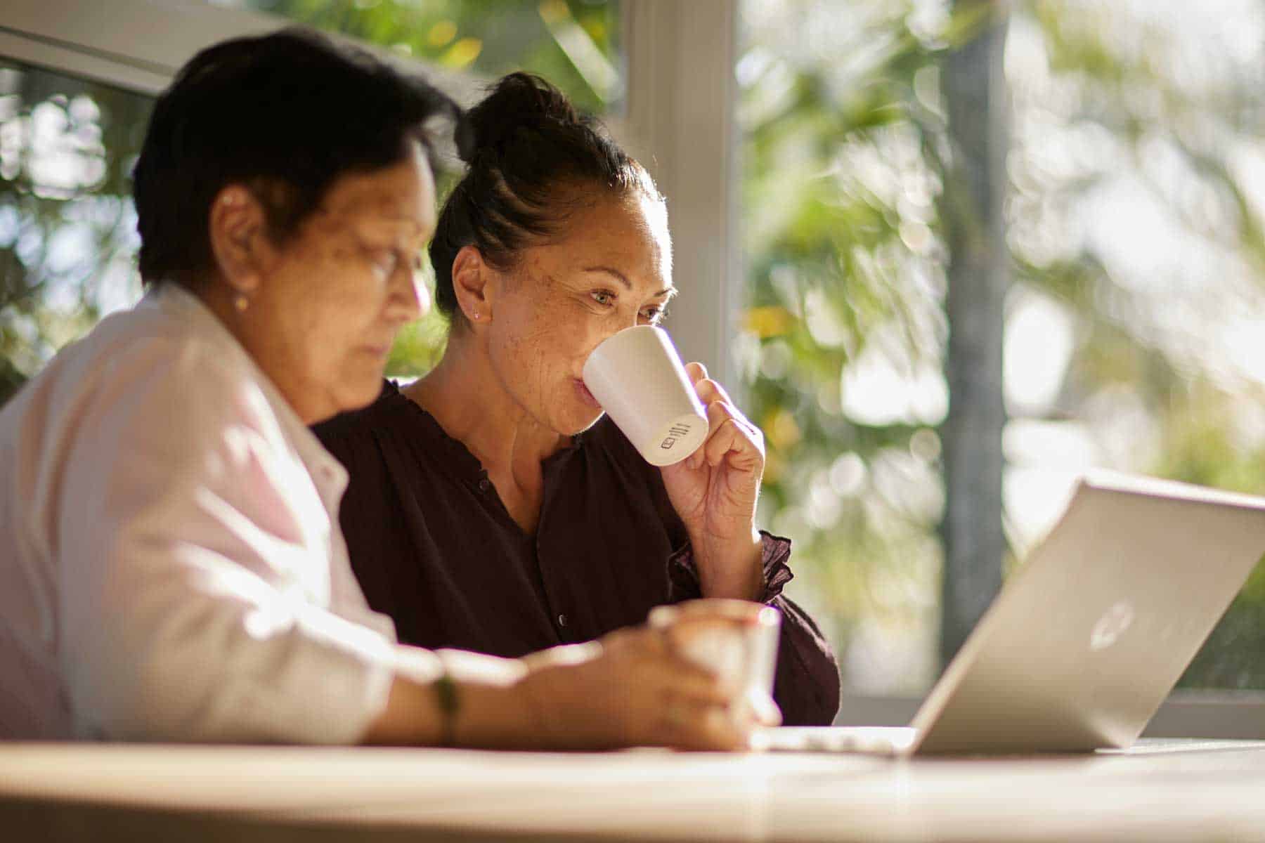 Two women reading a guide together on a laptop